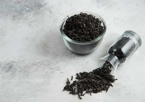 Dried pekoe tea in a glass cup with a tipped glass container and tea spilled on a counter. 