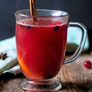 a glass mug with cranberry tea drink and a cinnamon stick