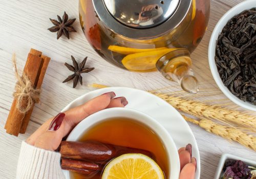 top-view-woman-hand-holding-cup-with-herbal-tea-with-cinnamon-lime-lemon-necessary-ingredients-white-background